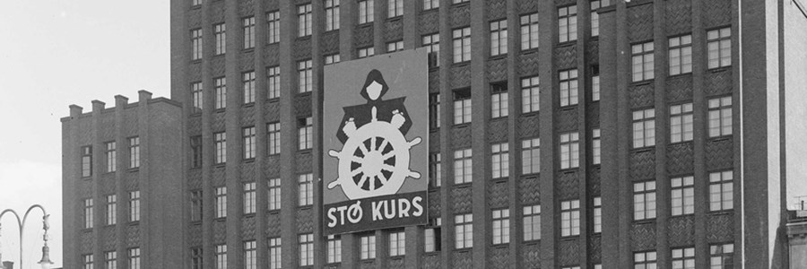 Folketeaterbygningen på Youngstorget med plakater for Arbeiderpartiplakater. Styrmann med ror med teksten "Stø kurs". Banner med teksten "Det norske arbeiderpartiet".
