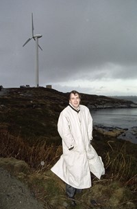 Mann med frakk står foran vindturbin. Mannen er Eivind Reiten som var olje- og energiminister i 1990 da bildet ble tatt. 