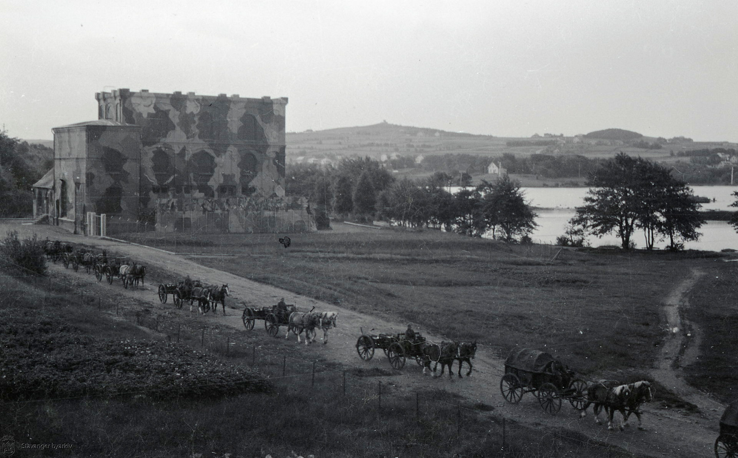 Et stort bygg med en rekke kjørende hest- og kjerrer i forgrunnen