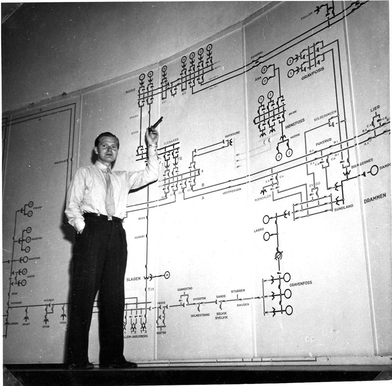 Mann peker på instrumenter på vegg i kontrollrom. 