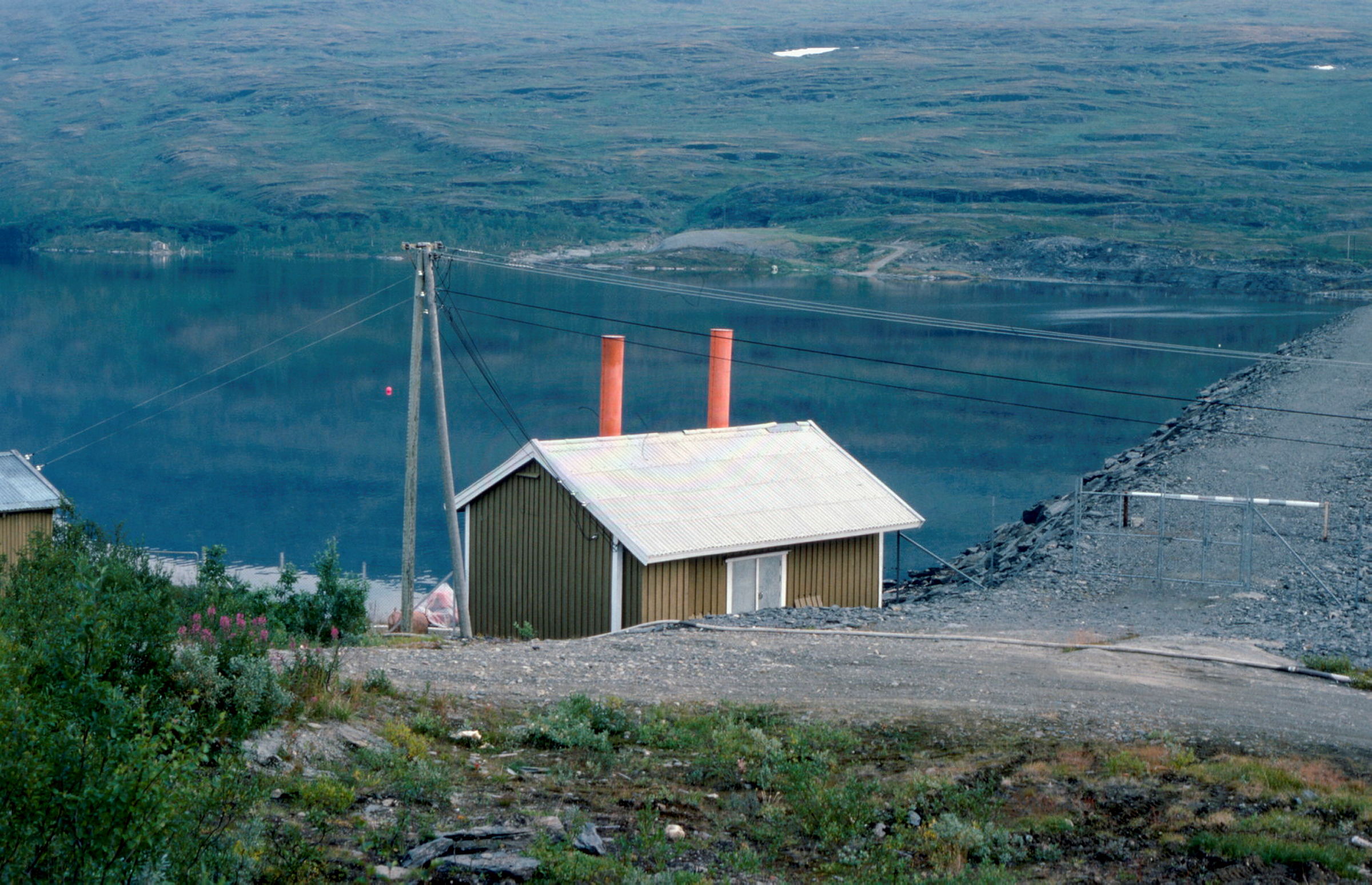 Trehus under en kraftledning foran et vann