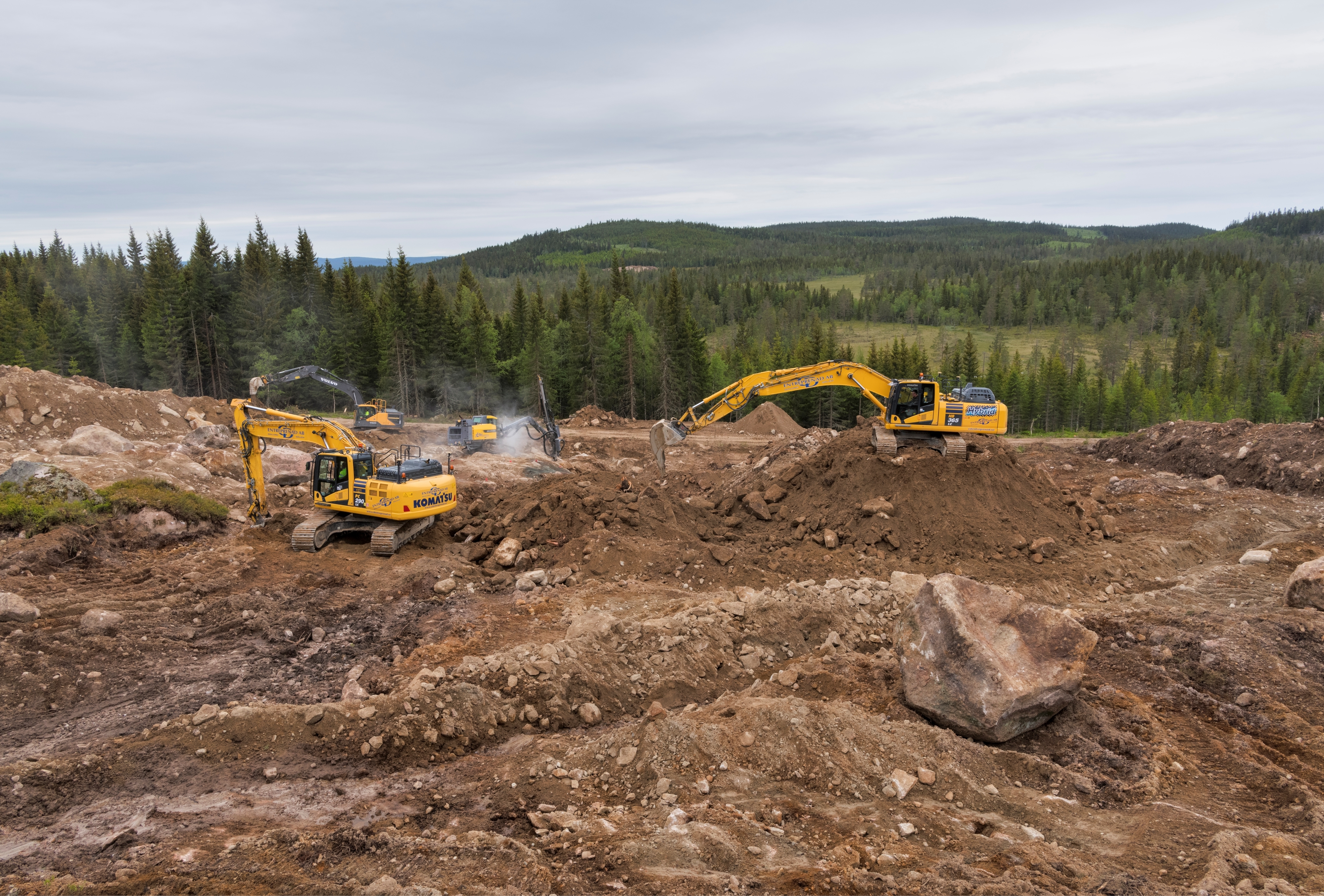 To gravemaskiner i arbeid på et masseuttak i skogen.