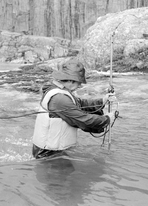 Mann står i stri elv med måleinstrument