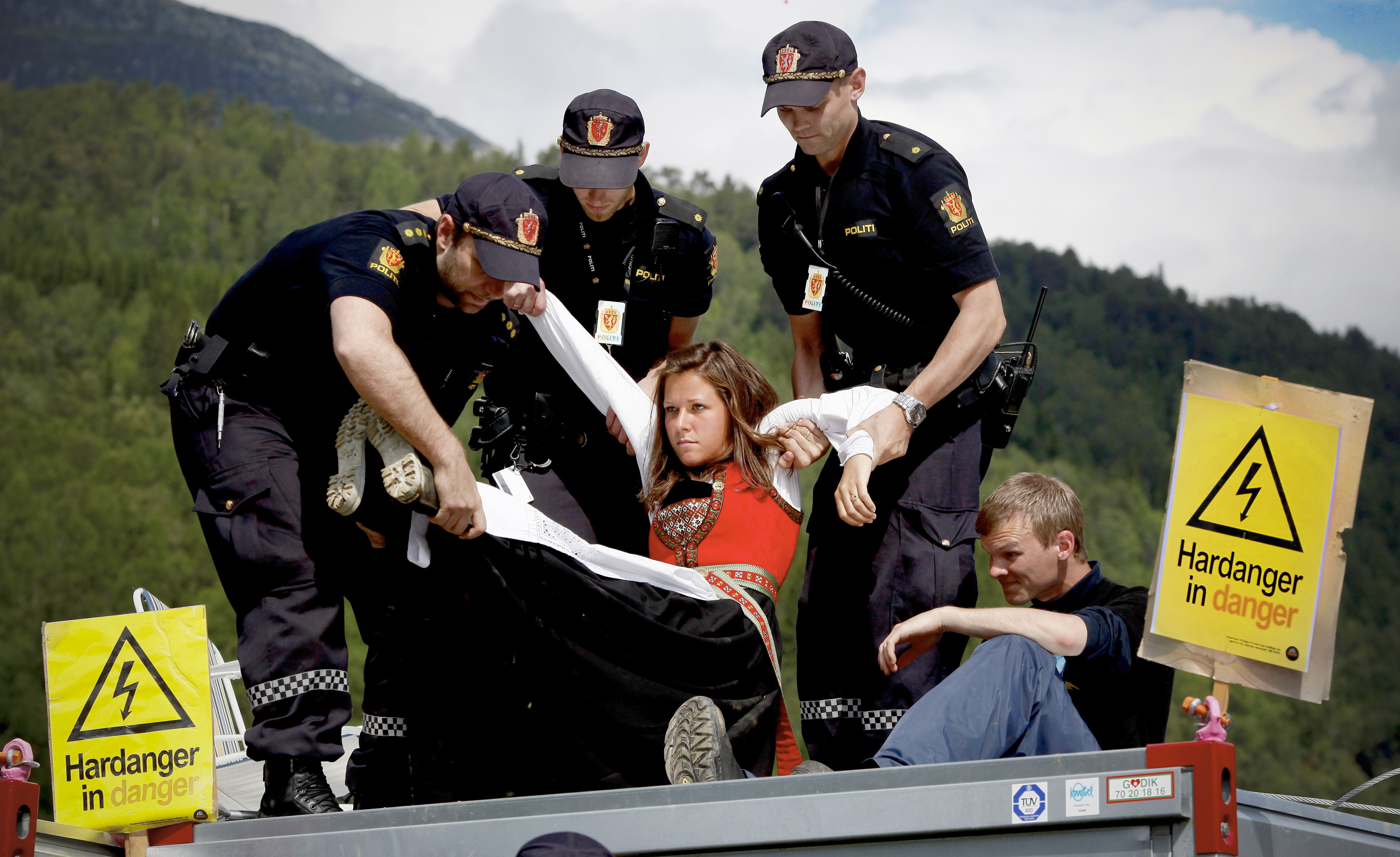 Ung kvinne i bunad blir båret bort av politi i uniform.