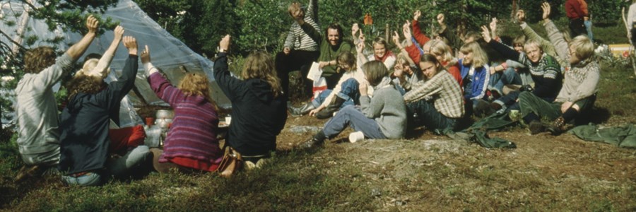 Personer sitter ved campingplass og tar håndsopprekning