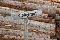 Skilt med påskrift Kjølberget foran tømmerstokker.