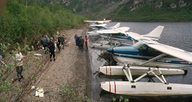 NVEs hovedstyre på befaring langs elvebredden. Småfly parkert i vannkanten.