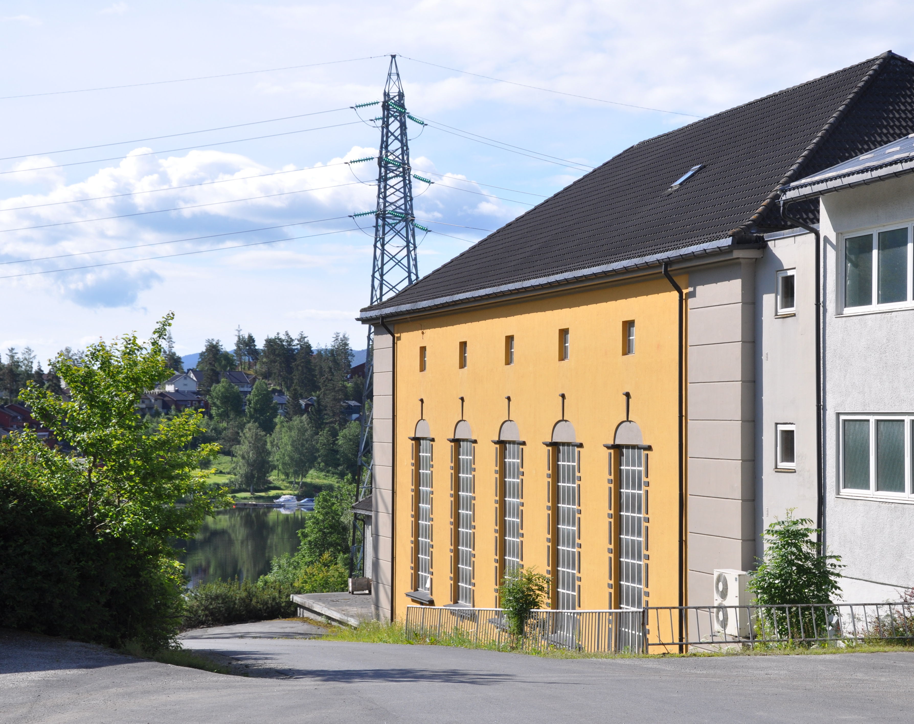 Transformatorstasjon med gulmalt fasade og kraftmast i bakgrunnen.  