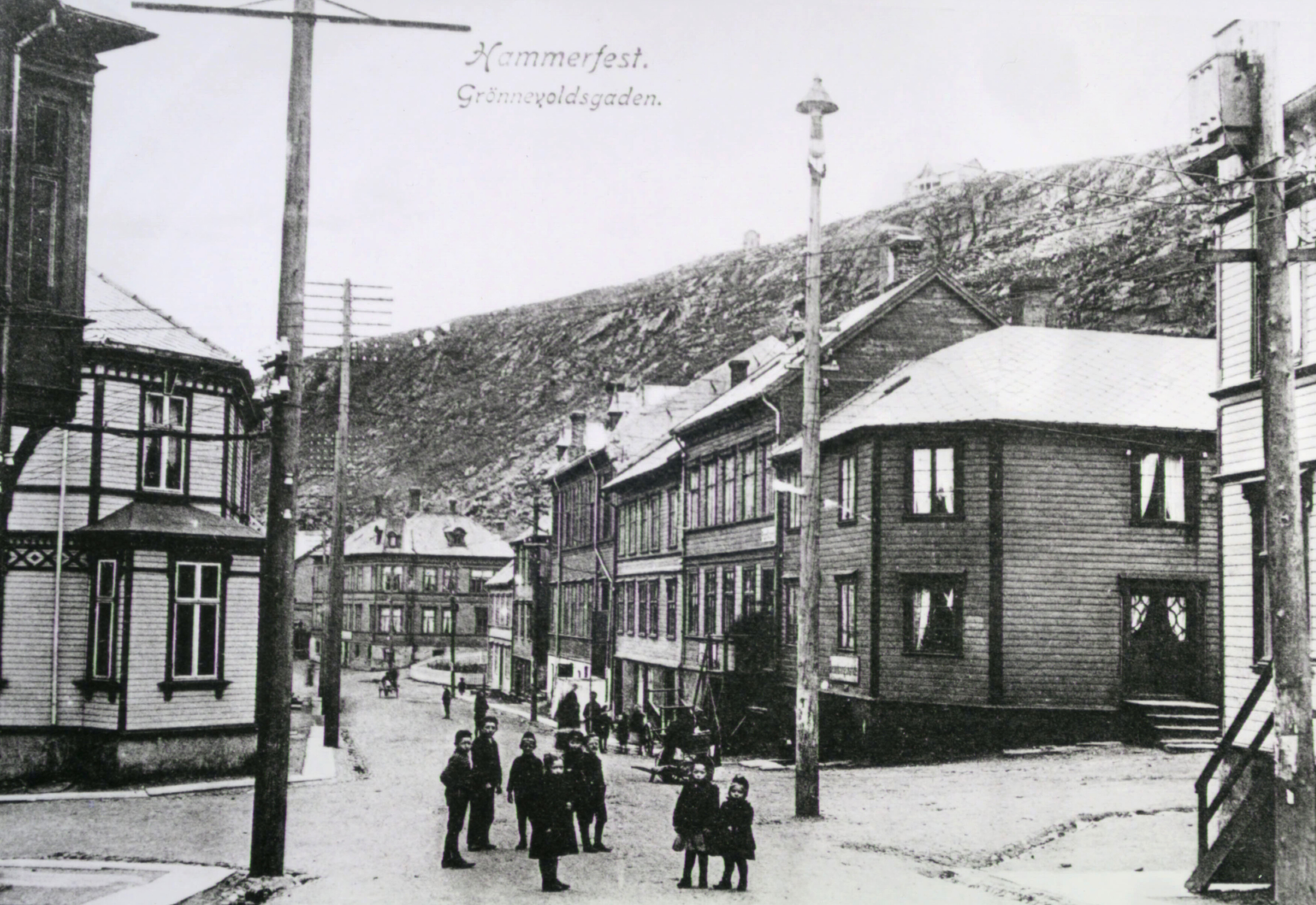 Gate med mennesker, trebygninger og trestolper.