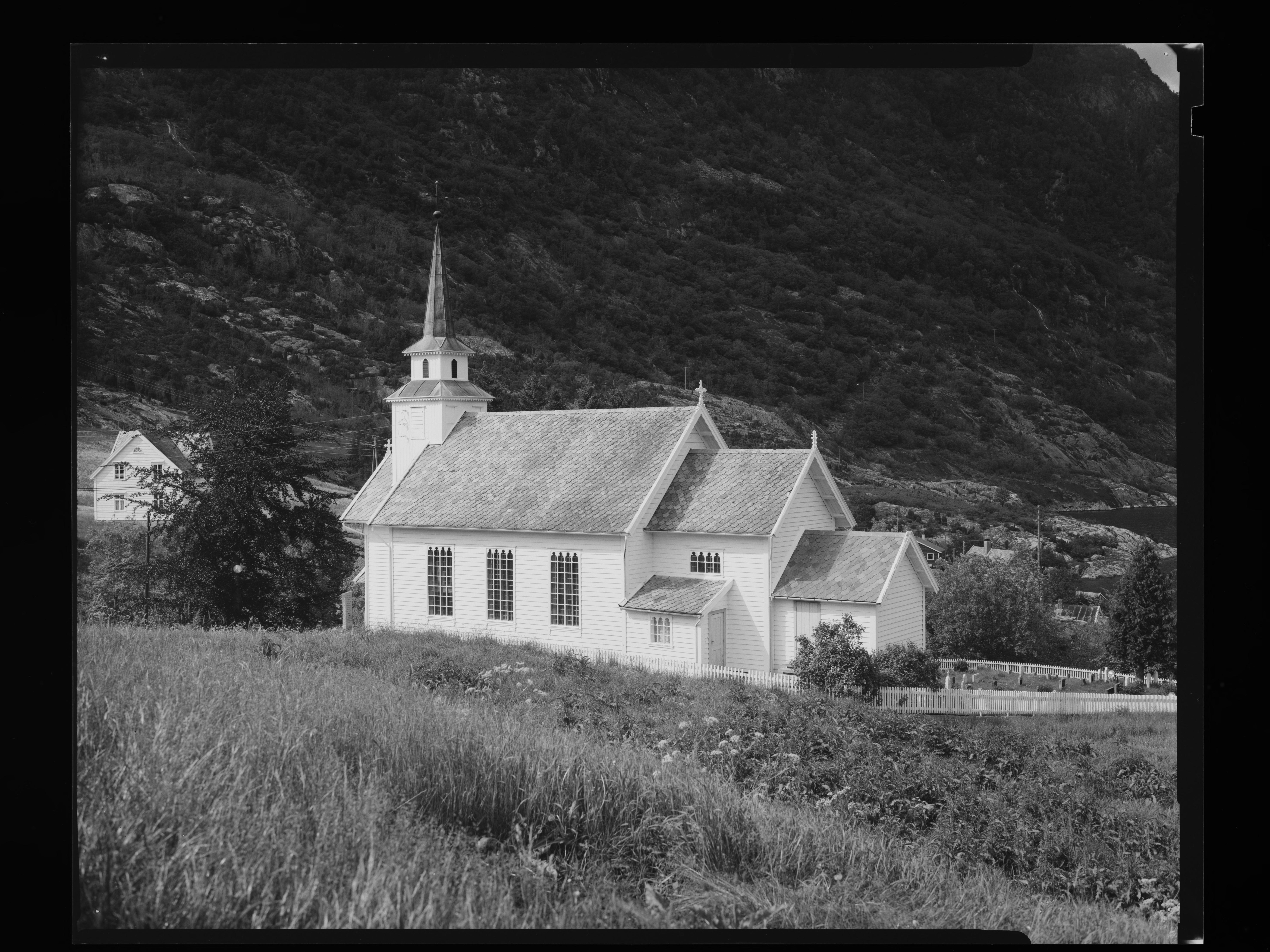 En sort-hvitt bilde av en kirke som står foran et fjell.