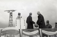 Fem menn står på et podium foran en vindturbin. To av mennene trykker på et teknisk apparat
