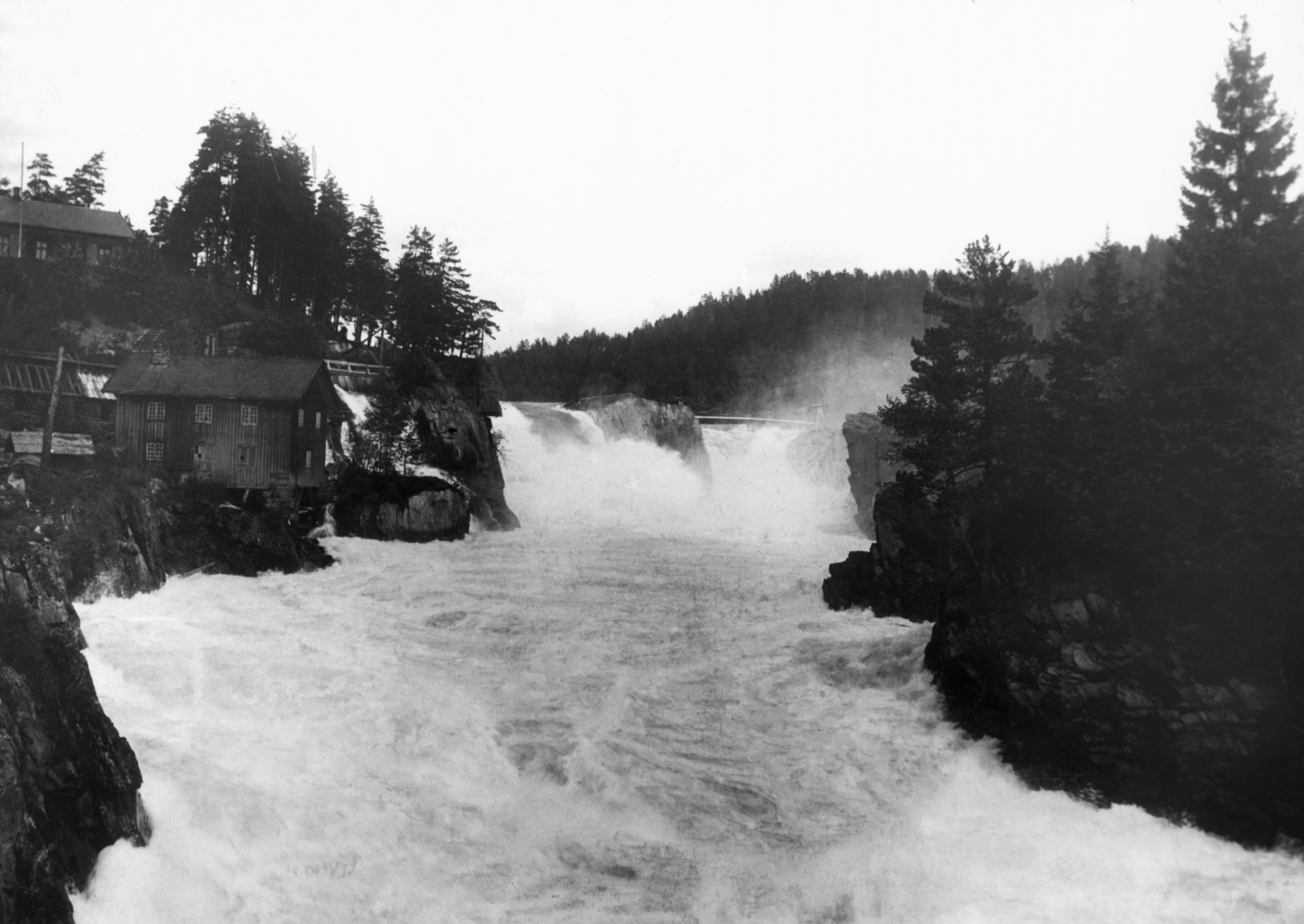 Flommende vann nedover en foss med bebyggelse ved siden av.