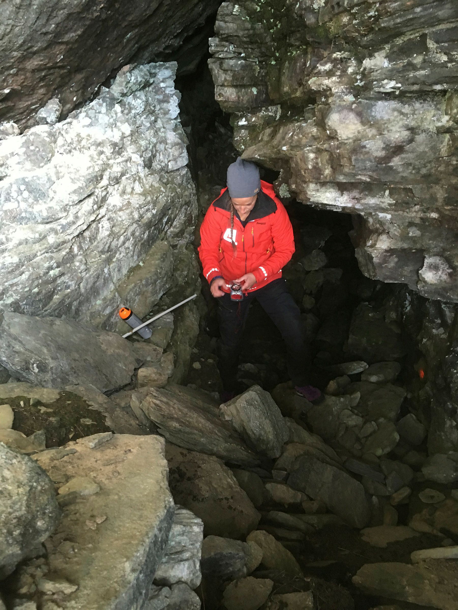 Person med rød NVE jakke inne i en fjellsprekk ser på kompass og gjør målinger.